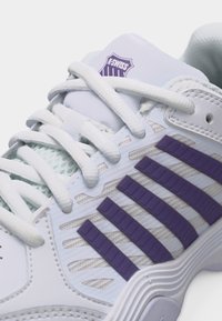 Λευκό παπούτσι K-Swiss με μοβ ρίγες, λευκά κορδόνια και λεπτομέρειες από δίχτυ στο πλάι και τη γλώσσα.