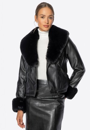 Veste en cuir noire avec un large col en fourrure et des poignets en fourrure. Le modèle est court, avec une fermeture éclair avant et deux poches latérales.