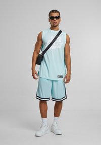 Haut sans manches bleu clair avec graphique blanc, shorts assortis, accents noirs, baskets blanches et un sac bandoulière noir.