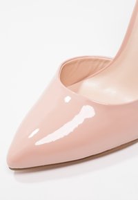 Chaussure à talon haut en cuir verni rose brillant avec un bout pointu et des côtés ouverts, présentant une surface lisse et brillante ainsi qu'une doublure intérieure neutre.