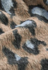 Gros plan sur un tissu beige doux avec un motif léopard irrégulier noir et gris clair.