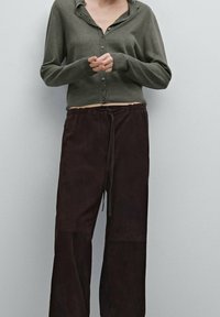 Donkergroene gebreide cardigan met knopen, gecombineerd met losse, bruine suède broek met een elastische tailleband en een trekkoord.