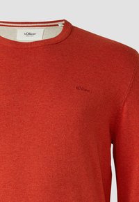 Roter Baumwollpullover mit rundem Ausschnitt, dezent strukturierter Oberfläche und kleinem Logo auf der Brust, ergänzt durch einen gestreiften inneren Kragen.