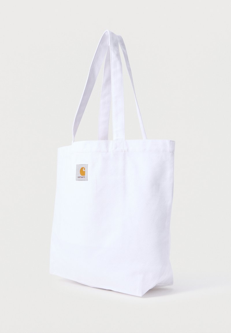 Sac fourre-tout en tissu blanc avec deux poignées et un petit patch logo Carhartt orange sur la partie supérieure avant.