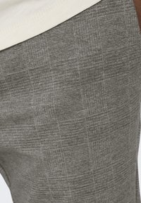 Tela gris texturizada de pantalones casuales, con un sutil patrón a cuadros, acabado suave y textura blanda.