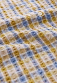 Tessuto a trama con un motivo a quadri giallo, blu e crema; presenta una superficie texture e bottoni bianchi per la chiusura.