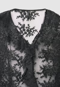Blusa nera trasparente con ricami floreali, scollo a V e dettagli arruffati. Tessuto morbido, motivi delicati e dettagli intricati in tutto il capo.