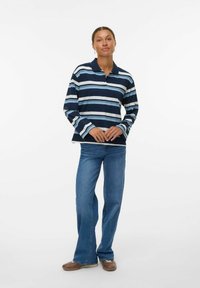Mörkblå och ljusblå randig långärmad polo med krage, tillsammans med utställda blå denimjeans och bruna skor.