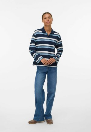 Navy and light blue striped long-sleeve polo shirt with a collared neck, paired with flared blue denim jeans and brown shoes.