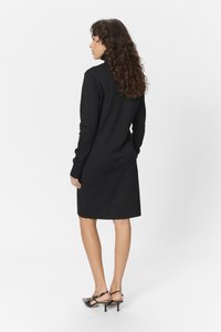 Black knitted dress with long sleeves, a high neckline, and a straight cut; worn with black heeled slingback shoes.