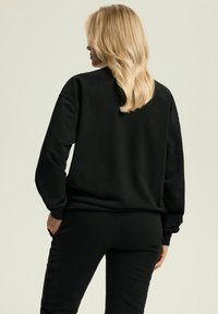 Czarna bluza z luźnym krojem, okrągłym dekoltem i długimi rękawami. Miękki materiał; zestawiona z czarnymi spodniami dla spójnego wyglądu.