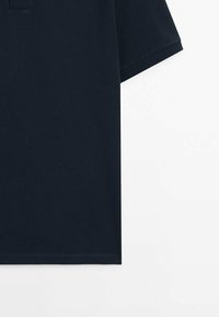 Polo shirt à manches courtes bleu marine foncé avec un tissu texturé, un col plat et une petite poche sur le côté gauche de la poitrine. Ourlet à coupe droite.