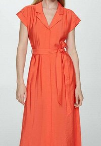 Różowa sukienka w odcieniu koralowym, wykonana z fakturowanej tkaniny, z kołnierzykiem, krótkimi rękawami, paskiem w talii oraz swobodnym krojem.
