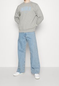 Gray sweatshirt with blue "NIKE" logo, paired with light blue wide-leg jeans and white sneakers. Material appears soft, casual design.