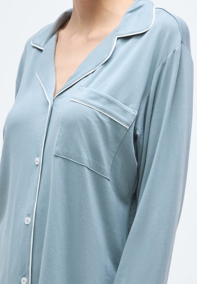 Világoskék pizsamafelső puha anyagból, gallérral, fehér szegéllyel, gombos záródással és egyetlen mellzsebbel.