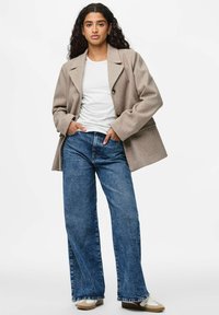 Kohvane villasegu üle suurte nööpidega bleiser, mida kantakse valge T-särgi üle ja sobitatakse siniste laia säärega teksade ja beežide tossudega.