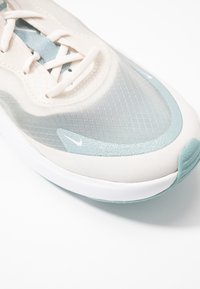 Nära bild av en beige och ljusblå sportskos tå med strukturerad ovandel, snören och en liten vit Nike-logotyp på sidan och sulan.