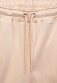 Beżowe szorty sportowe wykonane z gładkiego, lekkiego materiału, z elastycznym pasem i troczkami. Zawierają subtelne detale szycia.