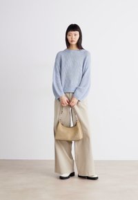 Un pull tricoté bleu clair avec des manches larges, un pantalon beige à jambes larges, et un petit sac tan avec un accent en argent. Des chaussures à plateforme noires.