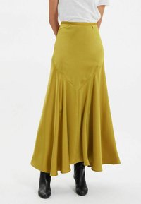 Jupe longue et fluide d'un jaune moutarde vibrant, confectionnée en tissu lisse. Dotée d'une taille haute et d'un design plissé pour plus de mouvement.