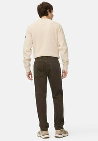 Cream ribbed sweater paired with dark brown pants, featuring a relaxed fit, side pockets, and a textured surface. Shoes are beige with accents.