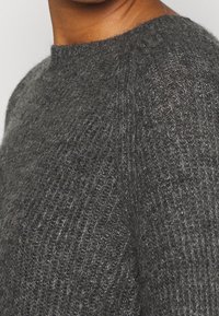 Pull gris tricoté avec un col rond, présentant un tissu texturé à tissage lâche et une apparence douce et légèrement duveteuse.