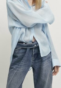 Ljusblå, genomskinlig skjorta med knappar i avslappnad passform och långa ärmar, kombinerad med mörka denimjeans med hög midja och lös passform.