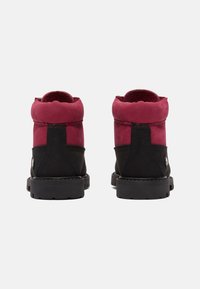 Botas de tobillo negras y burdeos con parte superior de ante, collar acolchado, suela gruesa de goma y puntera redondeada. Accentos de logo simples en el lateral.