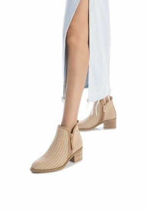 Stivaletti beige alla caviglia con una texture intrecciata, tacco basso a blocco e cerniere laterali; abbinati a una gonna di jeans chiara con uno spacco.