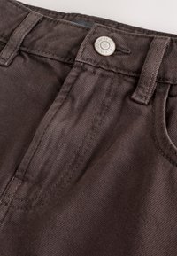 Pantaloni di denim marrone con vita standard dotata di bottone in metallo, tasca frontale e sottili dettagli di cucitura sul tessuto.