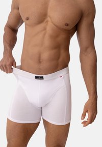 Bílé bavlněné boxerky s širokým elastickým pasem, na kterém je černá nášivka. Materiál má měkkou texturu a úzký střih.