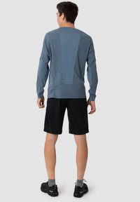 Lyseblå langermet topp med teksturert panel, kombinert med svarte shorts. Funksjoner inkluderer rundhals og oppbrettede ermer, brukt med joggesko.