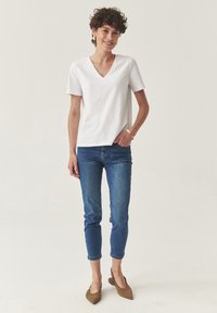 Camiseta blanca de manga corta y escote en V combinada con jeans azul ajustados y planos marrones con punta. Textura de tela suave y corte casual.