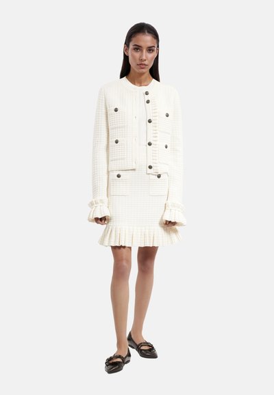 Ensemble en deux pièces texturé blanc comprenant une robe ajustée et une veste courte avec grands boutons, manches volantes et ourlet évasé.
