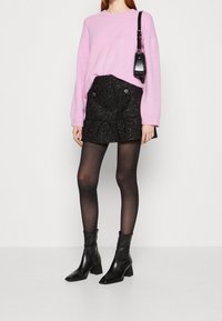 Personne portant un pull rose, une mini-jupe noire texturée, des collants noirs transparents, des bottines à talons noires et portant un petit sac à bandoulière noir.