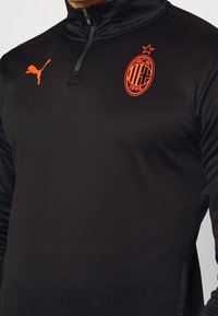 Maglietta sportiva nera a maniche lunghe con colletto a mezza zip. Presenta un logo Puma arancione e un'emblema AC Milan ricamato arancione.