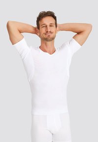White short-sleeve V-neck shirt made of smooth fabric, fitted design, with a seamless look. Model poses with arms raised.