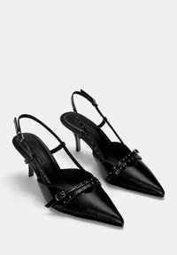 Čierne kožené slingback podpätky s prenikavými špičkami, strapcami s hrotmi a 3-palcovým stiletto podpätkom. Hladká textúra a nastaviteľný remienok okolo členka.