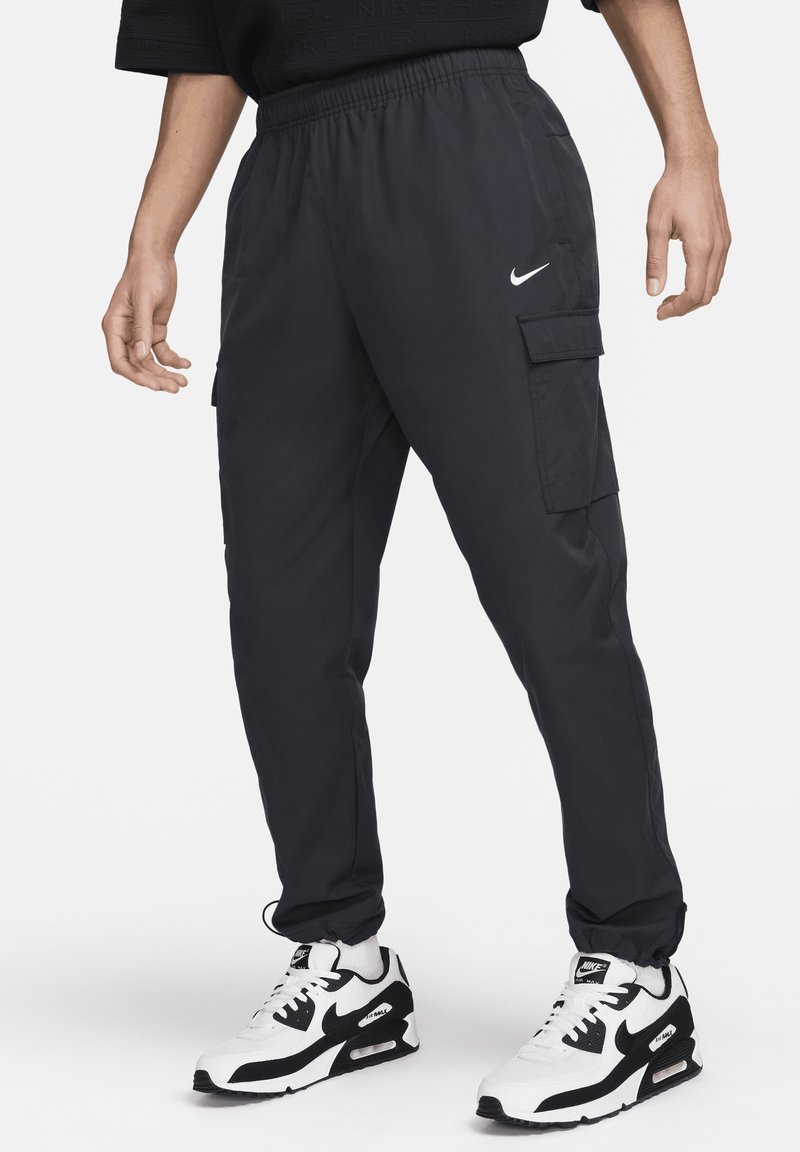 Černé cargo kalhoty s elastickým pasem, bočními kapsami a bílým logem Nike. Spojené s černobílými teniskami Nike.