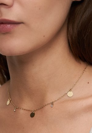 Goldene Halskette mit kleinen runden Anhängern und einem einzelnen Diamant-Akzent, die auf dem Schlüsselbein liegt. Glatte, polierte Oberfläche.