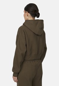 Felpa tagliata in tessuto verde oliva scuro, caratterizzata da un cappuccio, spalle abbassate e polsini a costine. La vestibilità è rilassata con una vita elasticizzata.
