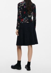 Floral long-sleeve top in black, red, and teal, paired with a dark blue flared skirt. The skirt features a textured finish. Black footwear.