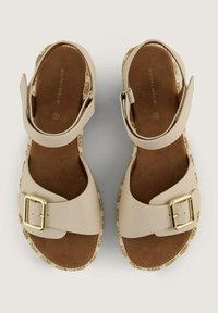 Beige Sandalen mit einem breiten Riemen und einer goldenen Schnalle, ausgestattet mit einer strukturierten braunen Wildledersohle und einer geflochtenen Jutesohle.