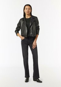 Schwarze Lederbikerjacke über einem dunkel gemusterten Oberteil, kombiniert mit schwarzen weit geschnittenen Jeans und Ankle Boots. Schlichte Hardware und elegantes Design.