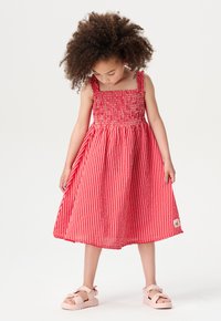 Rot-weiß gestreiftes Kleid mit quadratischem Ausschnitt und gerafftem Oberteil; knielang, kombiniert mit rosa Sandalen. Weicher Stoff, lässiges Design.