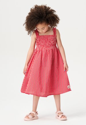 Robe rayée rouge et blanche avec un décolleté carré et un corsage froncé ; longueur au genou, associée à des sandales roses. Texture douce, design décontracté.