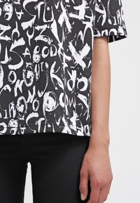 T-shirt nera a maniche corte con un motivo di testo astratto bianco. Il tessuto ha una consistenza liscia e una vestibilità comoda, con scollatura rotonda.