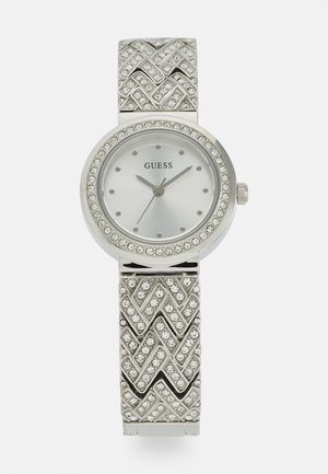 Zilveren Guess-horloge met een ronde wijzerplaat, een geaffineerde bezel en een textuur armband met een chevron-patroon en ingewerkte stenen.