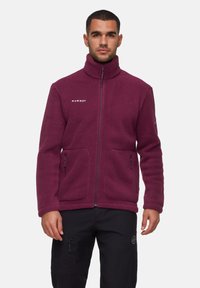 Giacca in polare bordeaux con colletto alto, chiusura con zip, due tasche frontali e logo sul petto. Presenta un materiale morbido e texturizzato.