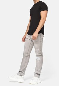 Jeans strappati grigi chiaro con vestibilità slim, realizzati in denim. Abbinati a una t-shirt nera attillata e sneakers bianche, con dettagli logorati.